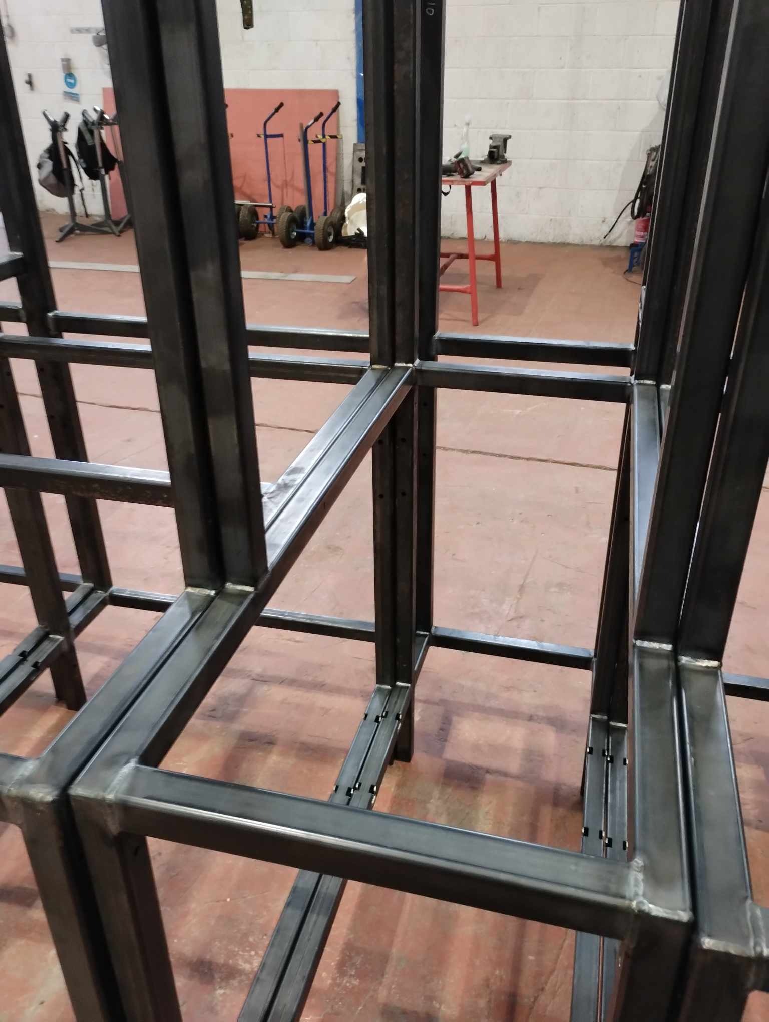 Surowa, spawana konstrukcja stalowa z profili zamkniętych, widoczne spawy, w tle wózek transportowy i narzędzia.