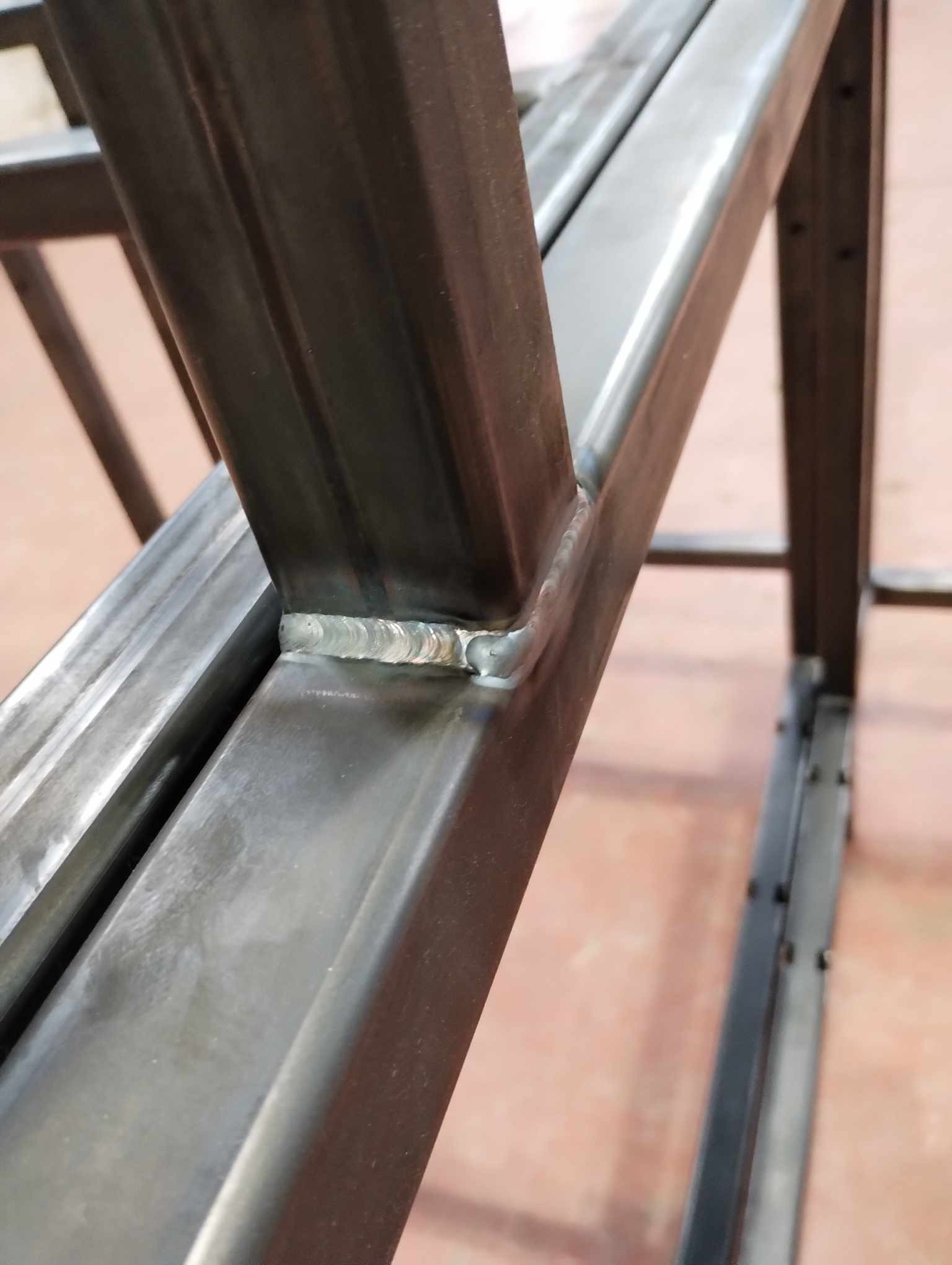 Szczegółowe ujęcie spawu łączącego metalowe profile konstrukcyjne pod kątem, widoczne ślady obróbki i niedoskonałości powierzchni.