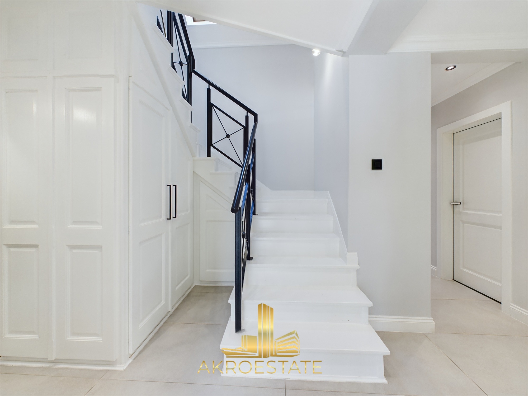 Jasne wnętrze domu: białe schody z czarną balustradą, wbudowana szafa i drzwi. Minimalistyczny design z dbałością o detale i oświetlenie.