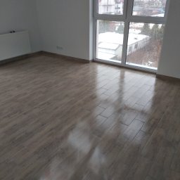 Michał Szatkowski - Ułożone panele podłogowe imitujące drewno w pustym pokoju z dużym oknem, za którym widać zimowy krajobraz.