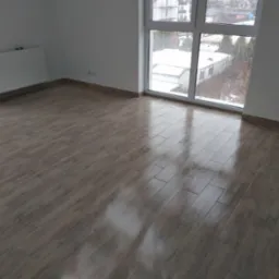 Ułożone panele podłogowe imitujące drewno w pustym pokoju z dużym oknem, za którym widać zimowy krajobraz.