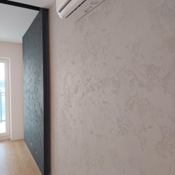 Firma usługowo-handlowa - Ściana z dekoracyjnym tynkiem strukturalnym w odcieniach beżu, z zamontowanym klimatyzatorem Haier, widoczna także część ściany w kolorze ciemnoszarym i fragment podłogi z paneli.