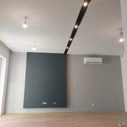 Firma usługowo-handlowa - Pomalowane na szaro ściany w pokoju z drewnianą podłogą, z ciemnoszarą dekoracyjną wstawką na ścianie i klimatyzacją, widoczne także oświetlenie sufitowe.