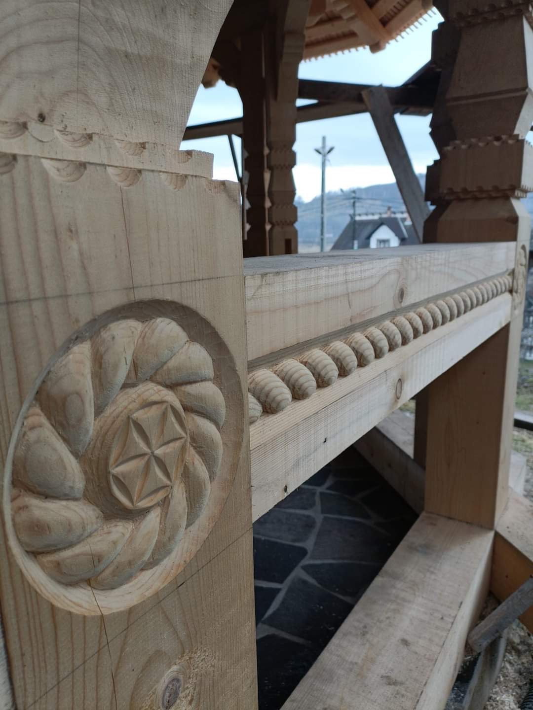 Drewniana konstrukcja dachu w trakcie budowy z widocznymi rzeźbieniami: rozetą i rzędem wypukłych elementów dekoracyjnych.