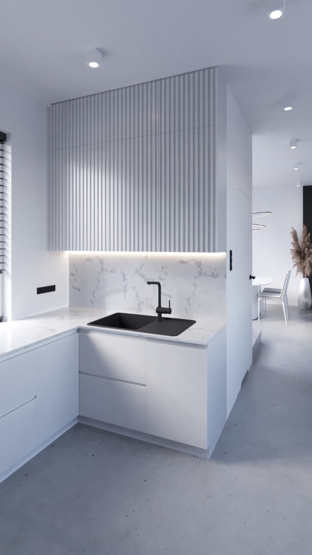 Minimalistyczna kuchnia z białymi szafkami, marmurowym blatem i czarną armaturą, oświetlona listwą LED pod szafkami wiszącymi z ryflowanymi frontami, widok na jadalnię z dekoracyjną trawą w wazonie.