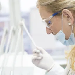 Stomatolog w okularach ochronnych i maseczce, w trakcie zabiegu, na pierwszym planie wiertło dentystyczne