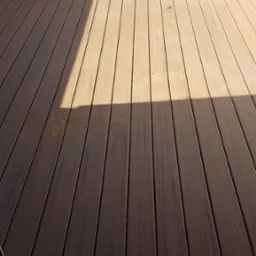 Montaż deski kompozytowej na tarasie, widoczna drabina oparta o ścianę i fragment osoby zamiatającej powierzchnię