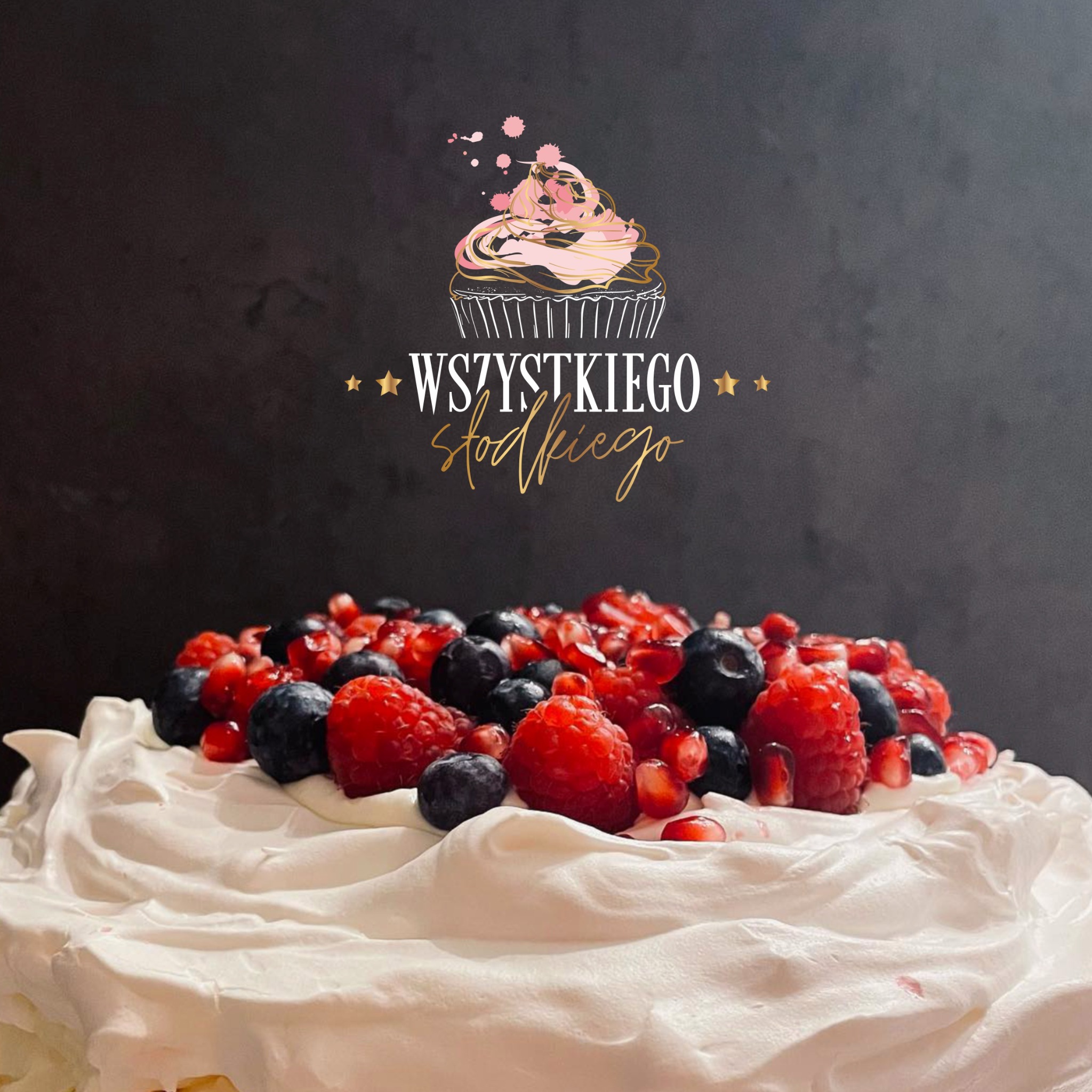 Tort bezowy udekorowany świeżymi malinami, borówkami i granatem, z napisem 'Wszystkiego słodkiego' i logo cukierniczym na ciemnym tle.