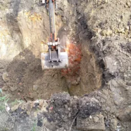 Koparka wykopuje dół z fragmentami starej ceglanej konstrukcji w ziemi.