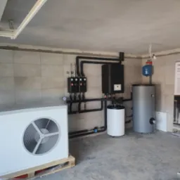 Zainstalowana pompa ciepła marki Stiebel Eltron na palecie w surowym wnętrzu, z widocznymi elementami instalacji grzewczej i zbiornikiem buforowym oraz plakatem informacyjnym.