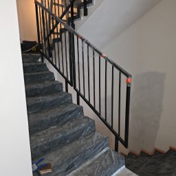TECHNOMAR Marcin Kaczmarek - Montaż czarnej, metalowej poręczy schodowej w Mysłowicach. Schody zabezpieczone folią, widoczne narzędzia. Minimalistyczny design, surowe wykończenie.