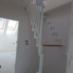 STYL -SPAW - Białe schody z balustradą w surowym wnętrzu, widoczne okno dachowe i instalacja elektryczna. Minimalistyczny design schodów.