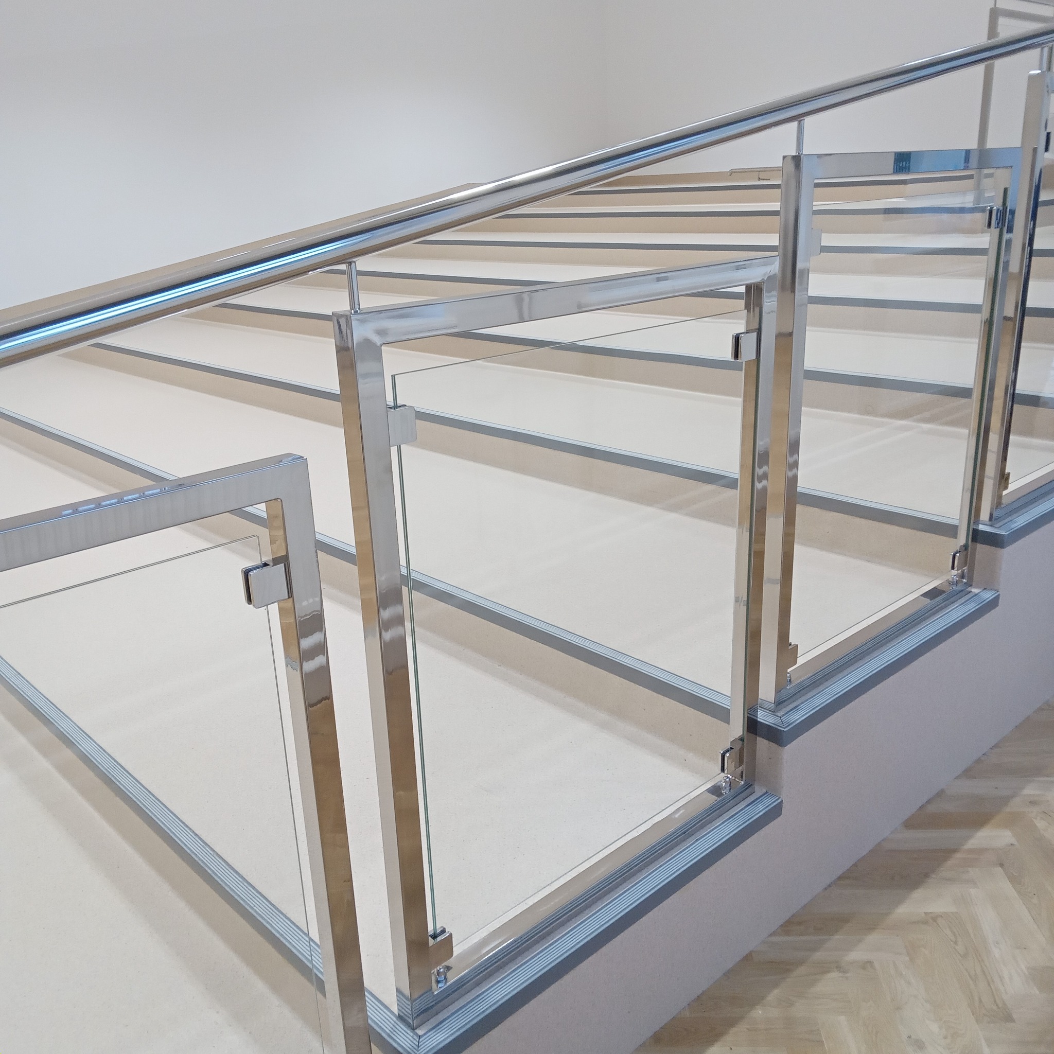 Nowoczesna balustrada schodowa ze stali nierdzewnej i szkła, minimalistyczny design, jasne wnętrze, widok z dołu, polerowane elementy.