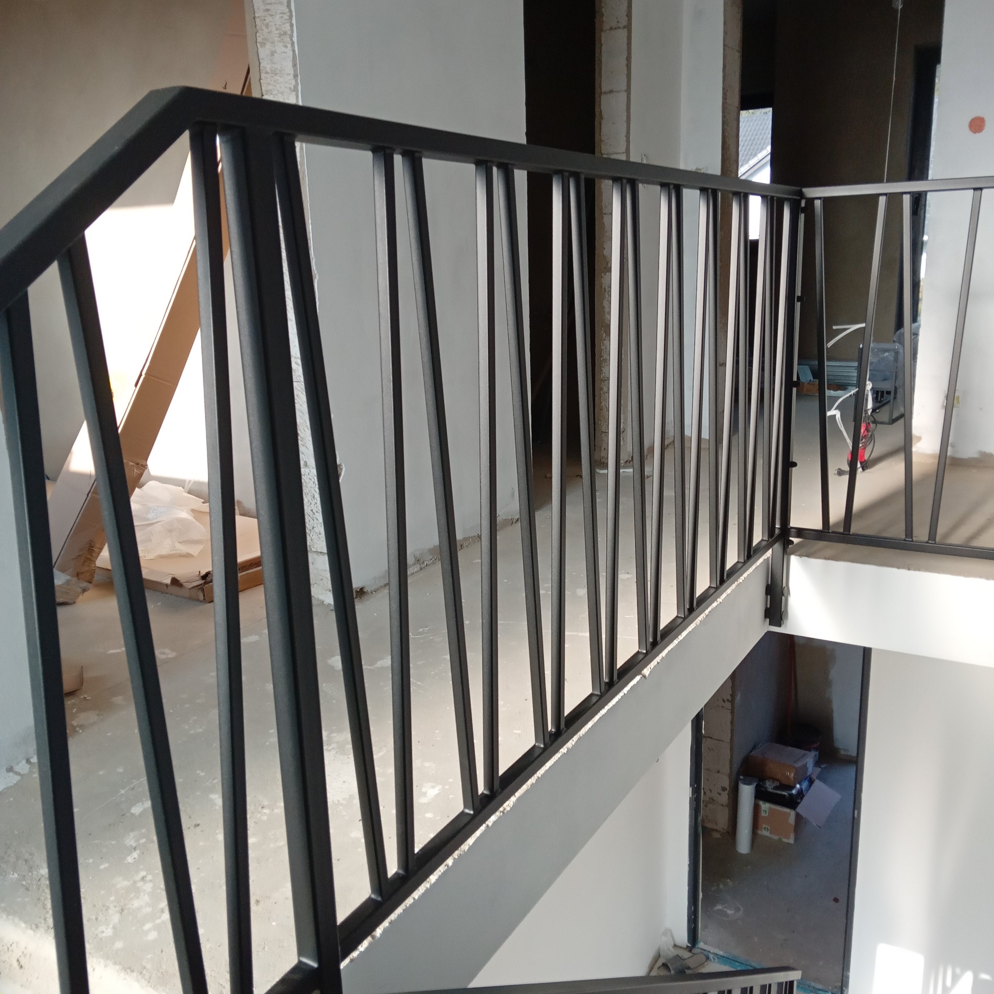 Nowoczesna, czarna balustrada metalowa z pionowymi szczebelkami na schodach w surowym wnętrzu. Widok z góry, detale wykończenia, minimalistyczny design.