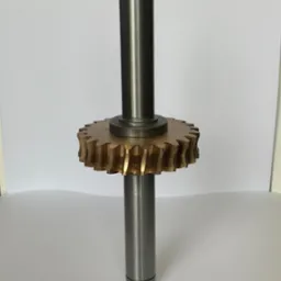 Wykonany z metalu wał z zębatką o skośnych zębach w kolorze złotym, sfotografowany na białym tle.