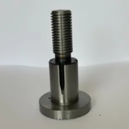 Metalowy uchwyt tokarski z gwintowanym trzpieniem i promieniowym nacięciem na cylindrycznej części, sfotografowany na jasnym tle.