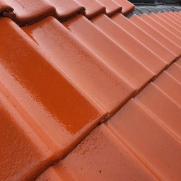 Dachy Czajkowscy - Michał Czajkowski - Błyszcząca, nowa dachówka ceramiczna w odcieniach czerwieni, ułożona równo na skośnym dachu, z widocznymi śladami wilgoci lub świeżo nałożonej impregnacji.