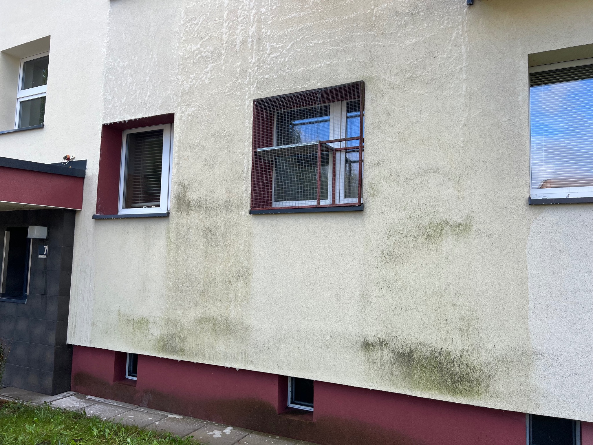 Fragment elewacji budynku z widocznymi śladami zabrudzeń i zacieków, z częściowo umytą powierzchnią, ukazującą różnicę w kolorze przed i po czyszczeniu.