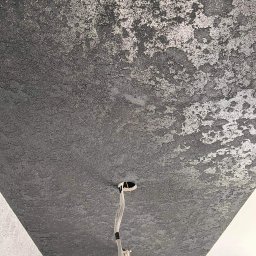 NOOK WYKOŃCZENIA WNĘTRZ KRYSTIAN ZYCH - Czarny sufit z dekoracyjną, srebrzystą strukturą, widoczne przewody elektryczne i otwór na oświetlenie.