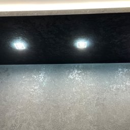 NOOK WYKOŃCZENIA WNĘTRZ KRYSTIAN ZYCH - Czarny sufit z fakturą i trzema wbudowanymi punktami świetlnymi nad szarą ścianą z efektem dekoracyjnym.