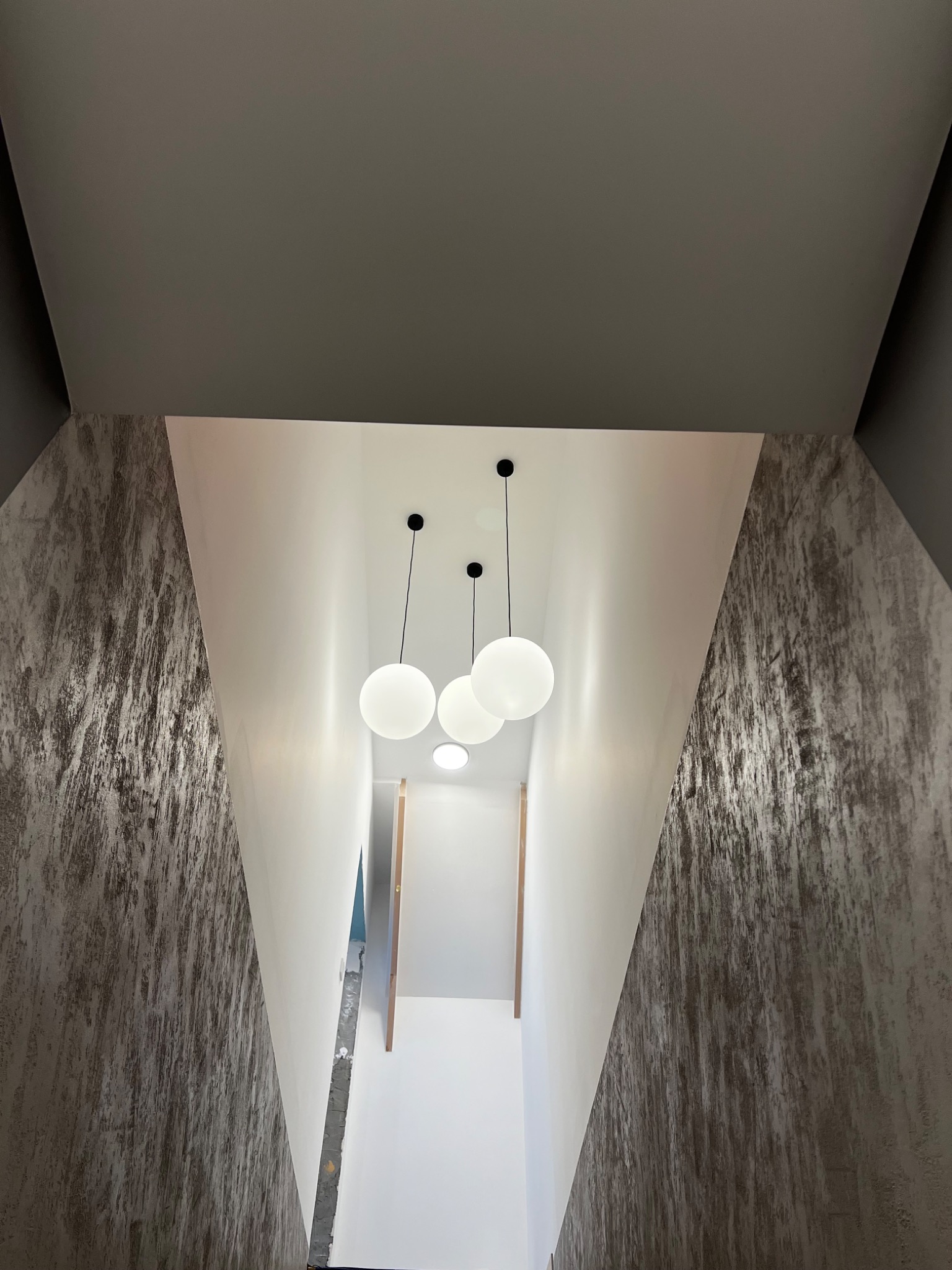 Korytarz po remoncie z dekoracyjną strukturą na ścianach w odcieniach szarości i trzema okrągłymi lampami wiszącymi na białym suficie.