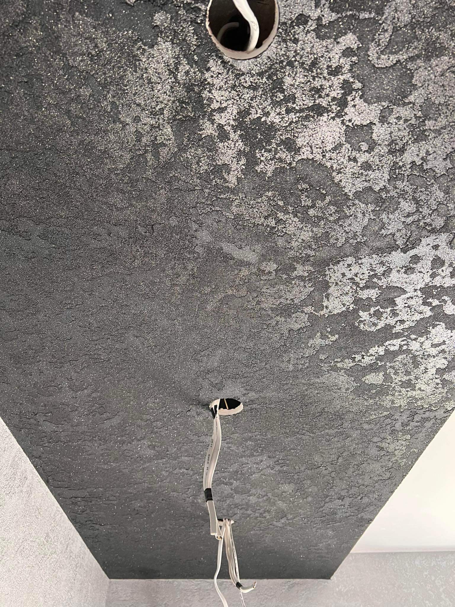 Czarny sufit z dekoracyjną, srebrzystą strukturą, widoczne przewody elektryczne i otwór na oświetlenie.