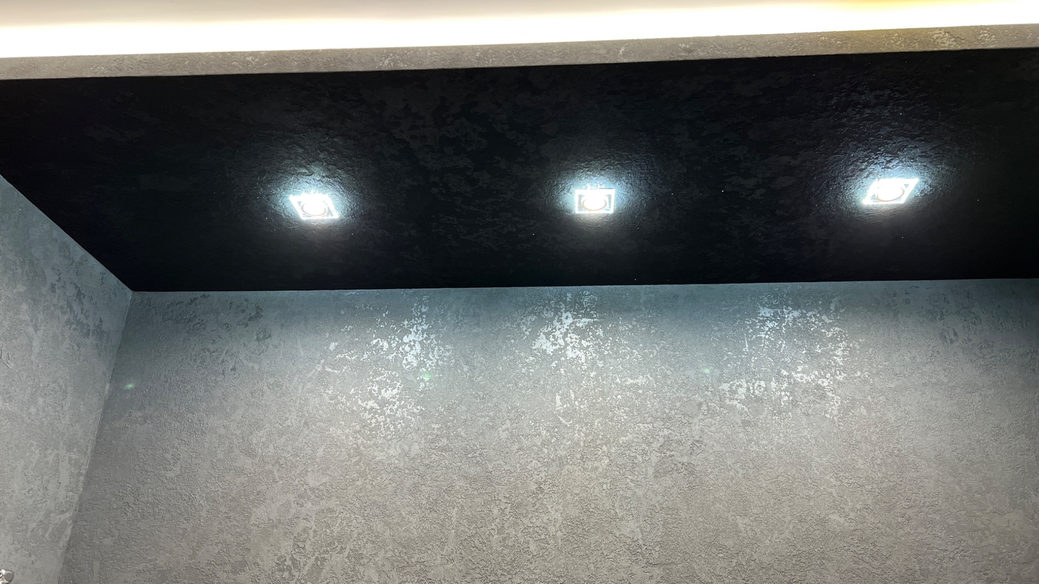 Czarny sufit z fakturą i trzema wbudowanymi punktami świetlnymi nad szarą ścianą z efektem dekoracyjnym.