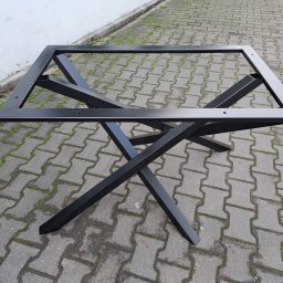 MARZOS Agnieszka Gołąb - Czarna, metalowa podstawa stołu z krzyżowymi nogami i ramą mocującą blat, sfotografowana na brukowanej nawierzchni w Warszawie.