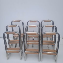 MARZOS Agnieszka Gołąb - Rząd identycznych, składanych drabinek ze stali nierdzewnej z drewnianymi stopniami, ustawionych na białym tle.