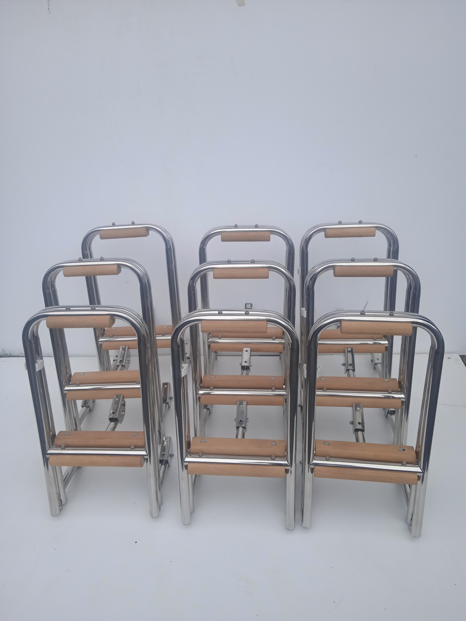 Rząd identycznych, składanych drabinek ze stali nierdzewnej z drewnianymi stopniami, ustawionych na białym tle.