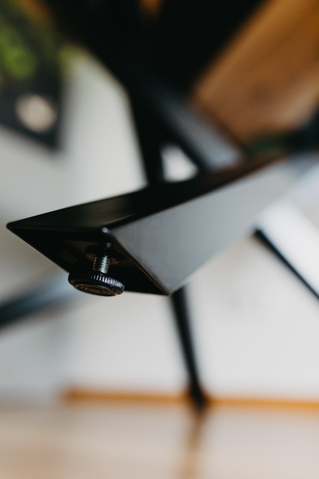 Szczegół czarnej, metalowej nogi stołu z regulowaną stopką, widoczna faktura metalu i gwint śruby.