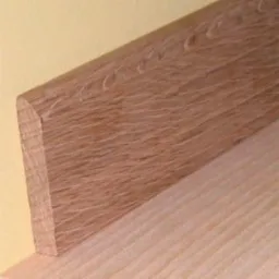 Profilowana listwa przypodłogowa z drewna dębowego, widoczna struktura usłojenia, zamontowana przy ścianie. Cokół wykończeniowy.