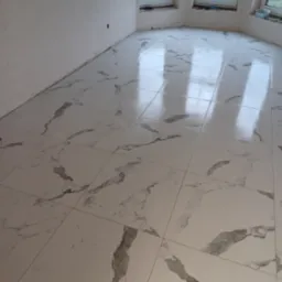 Połyskująca podłoga z białych płytek imitujących marmur, świeżo ułożona w jasnym pomieszczeniu z trzema oknami, widoczne odbicie okien w płytkach.