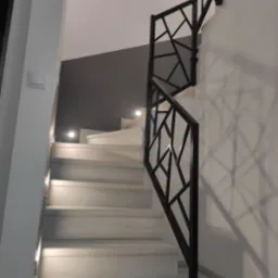 Nowoczesne schody z białymi stopniami i czarną, geometryczną balustradą, oświetlone punktowymi lampkami w ścianie.