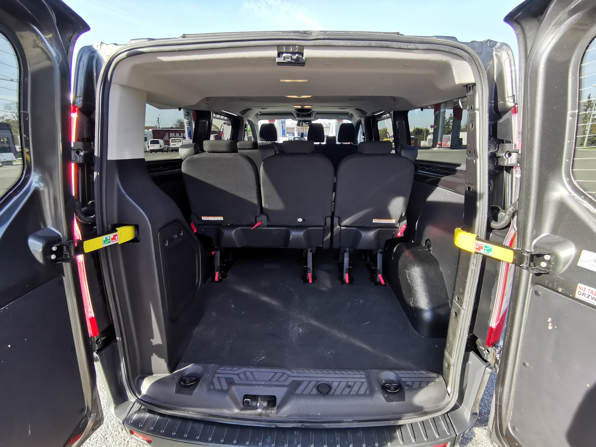 Wnętrze busa pasażerskiego z otwartymi drzwiami bagażnika, widoczne trzy rzędy siedzeń i pusta przestrzeń bagażowa.