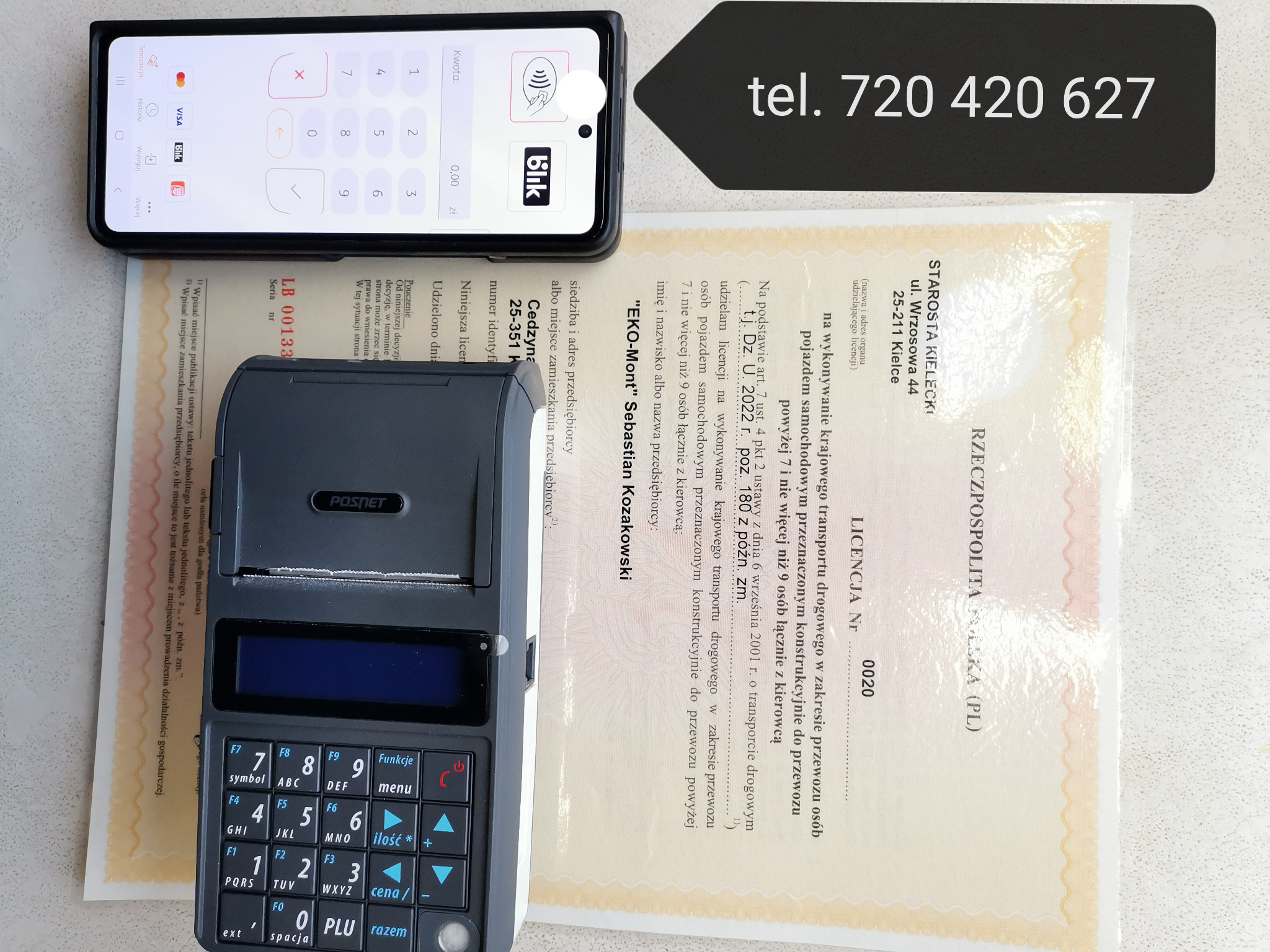Licencja na przewóz osób z terminalem płatniczym i telefonem z aplikacją bankową, numer telefonu nad licencją.