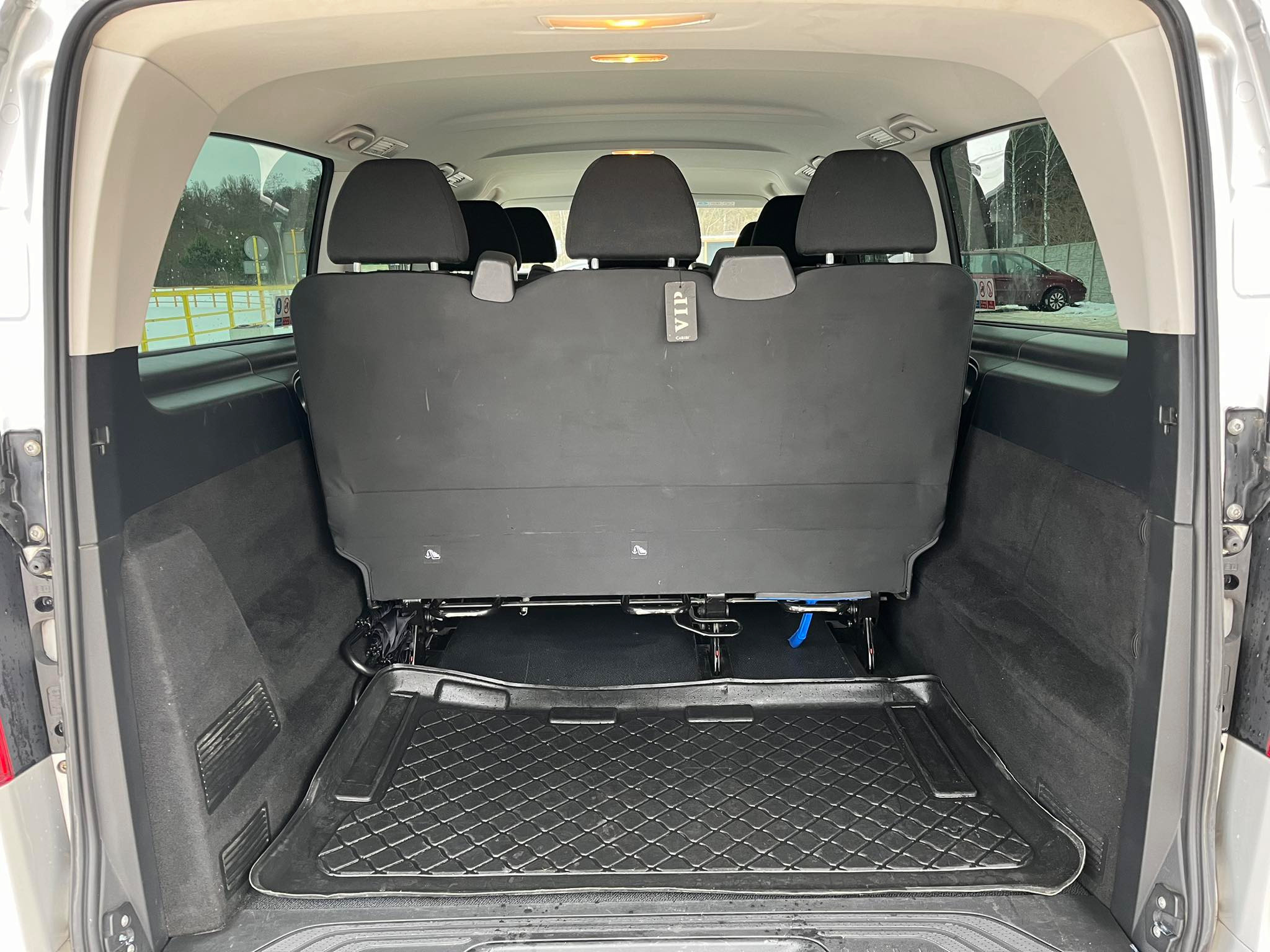 Wnętrze busa VIP z widocznymi czarnymi siedzeniami i gumową wycieraczką w bagażniku, z zewnątrz widoczny zimowy krajobraz.