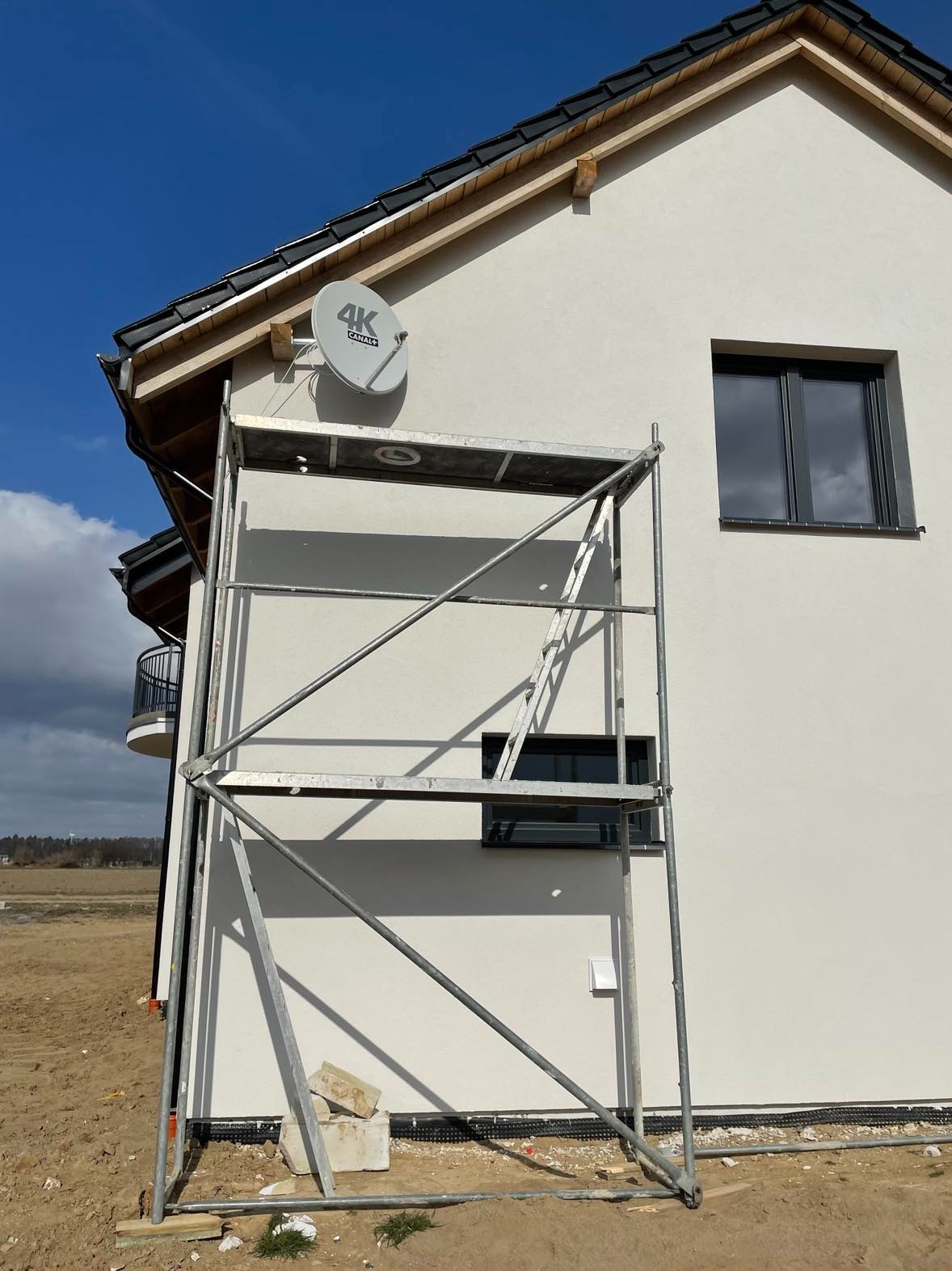Szara antena satelitarna 4K Canal+ zamontowana na jasnej elewacji domu jednorodzinnego, widoczna z rusztowania.