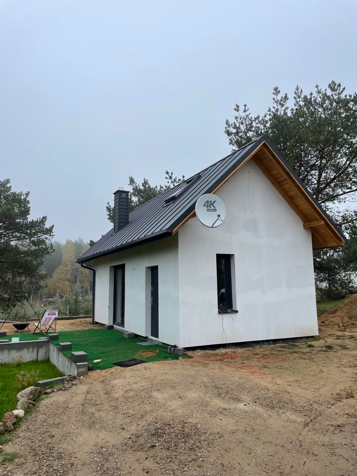 Nowoczesny dom jednorodzinny z zamontowaną anteną satelitarną 4K Canal+ na elewacji, widok z boku na tle pochmurnego nieba i drzew.