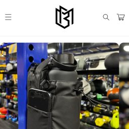 Igor Pieczyński - Zdjęcie z ekranu telefonu prezentujące czarny bidon w torbie z kieszenią na telefon, zawieszone na niebieskim stojaku na tle sprzętu do ćwiczeń. Na górze ekranu widoczny baner reklamowy Black Friday.