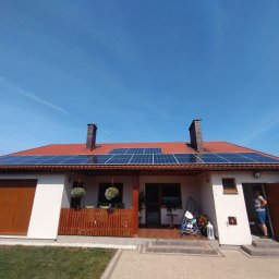 TO GLORY Oleh Blahodyr - Dom jednorodzinny z panelami słonecznymi na czerwonym dachu, widok z przodu, błękitne niebo, osoba w drzwiach, częściowo widoczny biały bus z napisem.