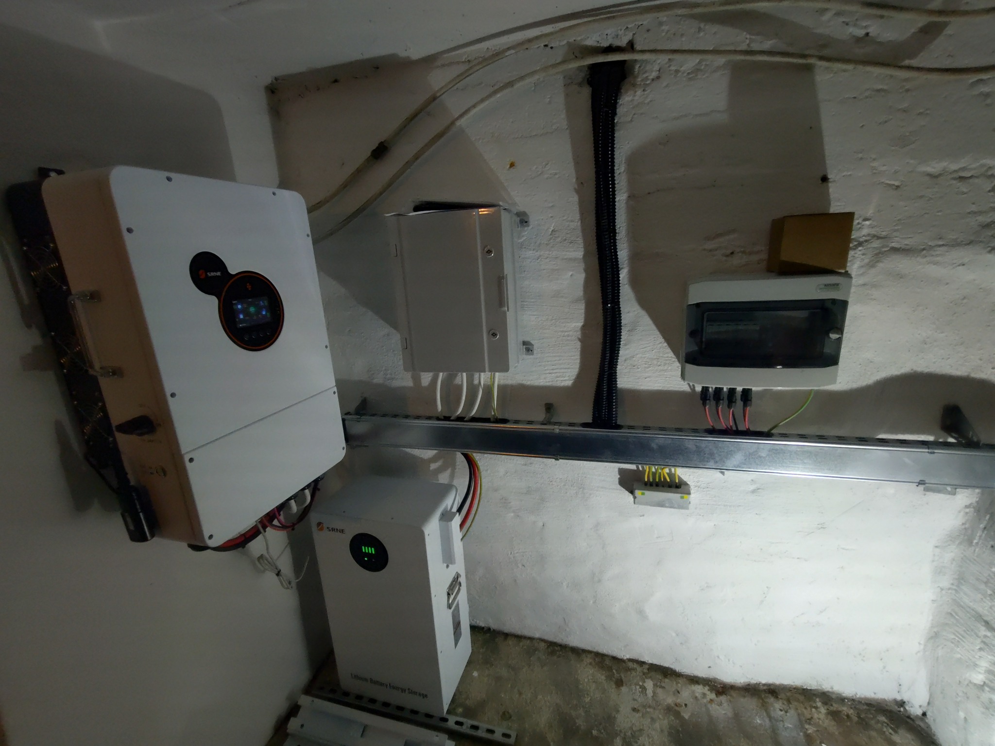 Zamontowany inwerter fotowoltaiczny SRNE z podłączonym akumulatorem energii na ścianie z instalacją elektryczną i zabezpieczeniami. Widok z dołu.