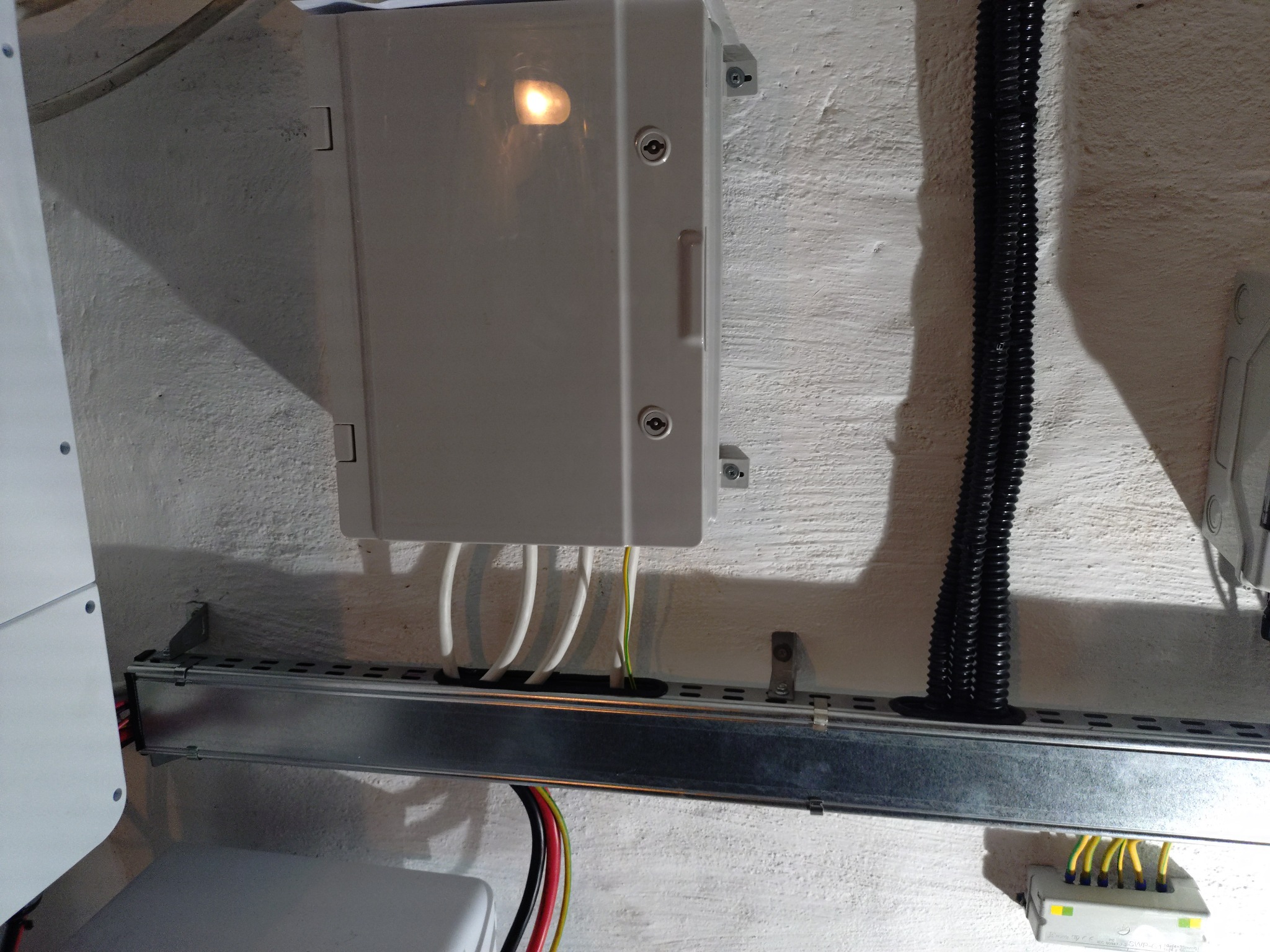 Zamknięta skrzynka elektryczna na ścianie z wyprowadzonymi przewodami. Widoczna szyna montażowa i peszel. Oświetlenie wewnątrz skrzynki.