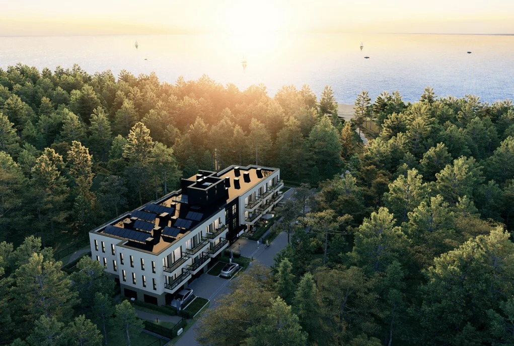 Klimatyczny apartamentowiec z panelami solarnymi na dachu, otoczony lasem, z widokiem na morze i żaglówki o zachodzie słońca. Ujęcie z lotu ptaka.