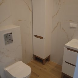 MARIO-BUD - Nowoczesna łazienka z beżowymi płytkami imitującymi marmur, białą zabudową WC, wysoką szafką i umywalką z szufladami. Drewnopodobna podłoga.