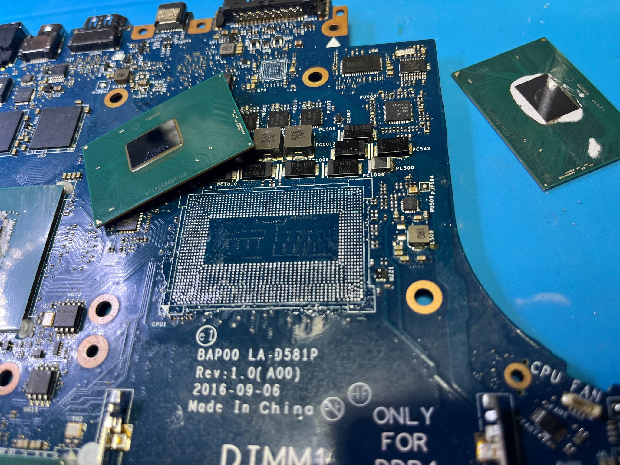 Płyta główna laptopa z dwoma procesorami, jeden zielony leży obok gniazda, drugi z resztkami pasty termoprzewodzącej obok, widoczne oznaczenia BAP00 LA-D581P i Made in China.