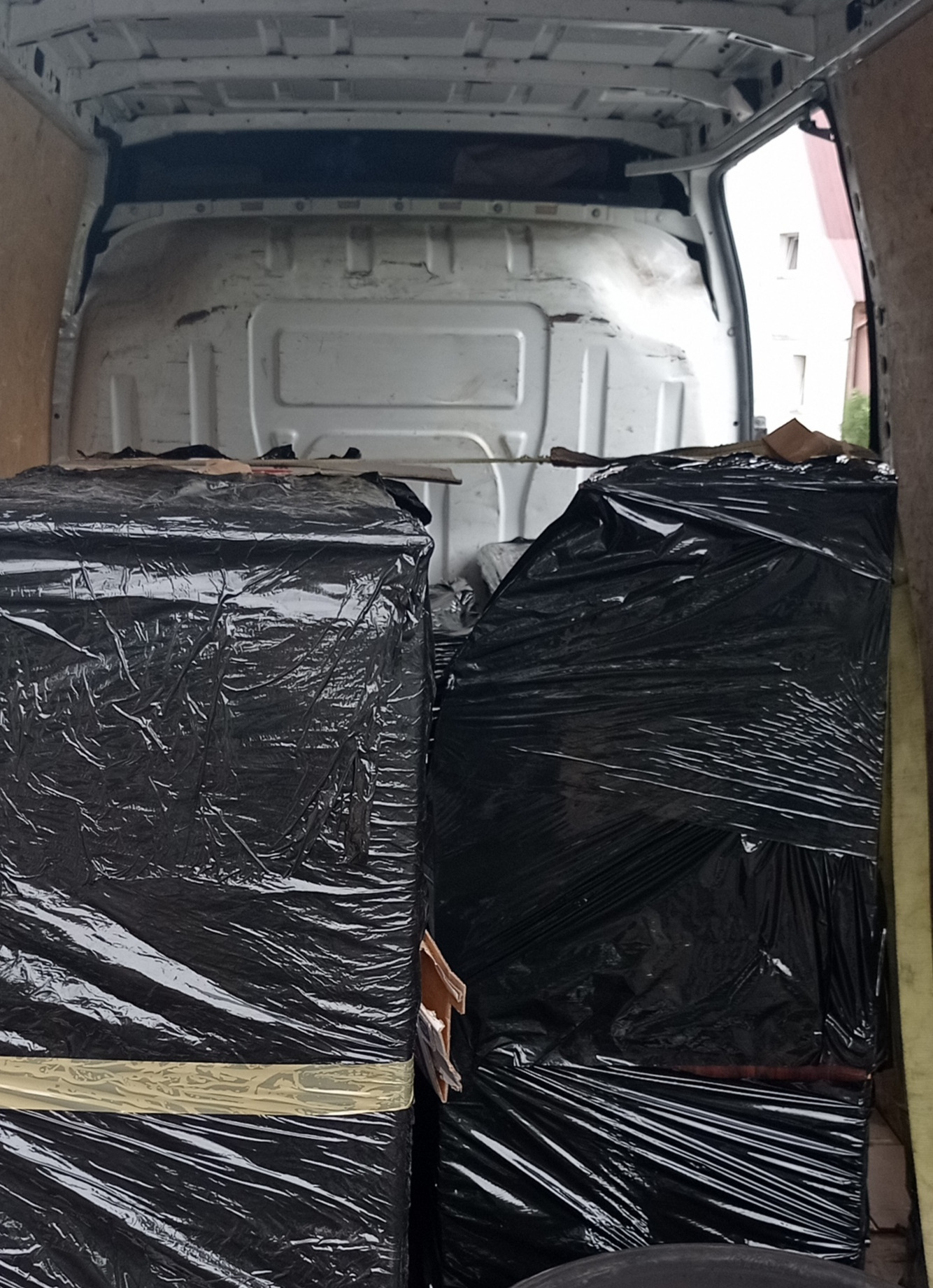 Wnętrze furgonetki z załadowanymi paczkami owiniętymi czarną folią stretch, zabezpieczonymi taśmą, gotowymi do transportu.