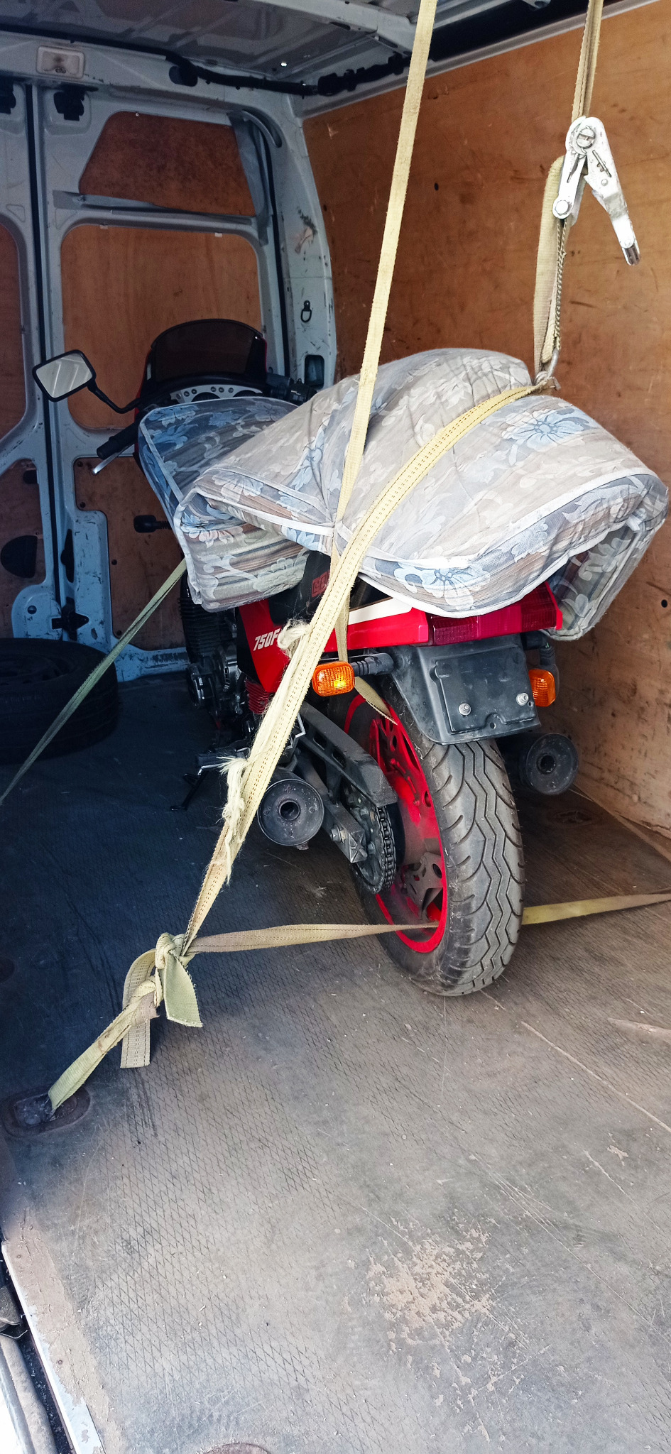 Czerwony motocykl 750F zabezpieczony pasami transportowymi i przykryty wzorzystą kołdrą wewnątrz furgonetki.