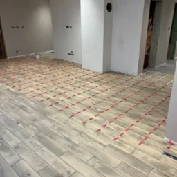 Układanie podłogi z płytek imitujących drewno z użyciem czerwonych krzyżyków dystansowych; widoczne przygotowane, surowe ściany i instalacje elektryczne.