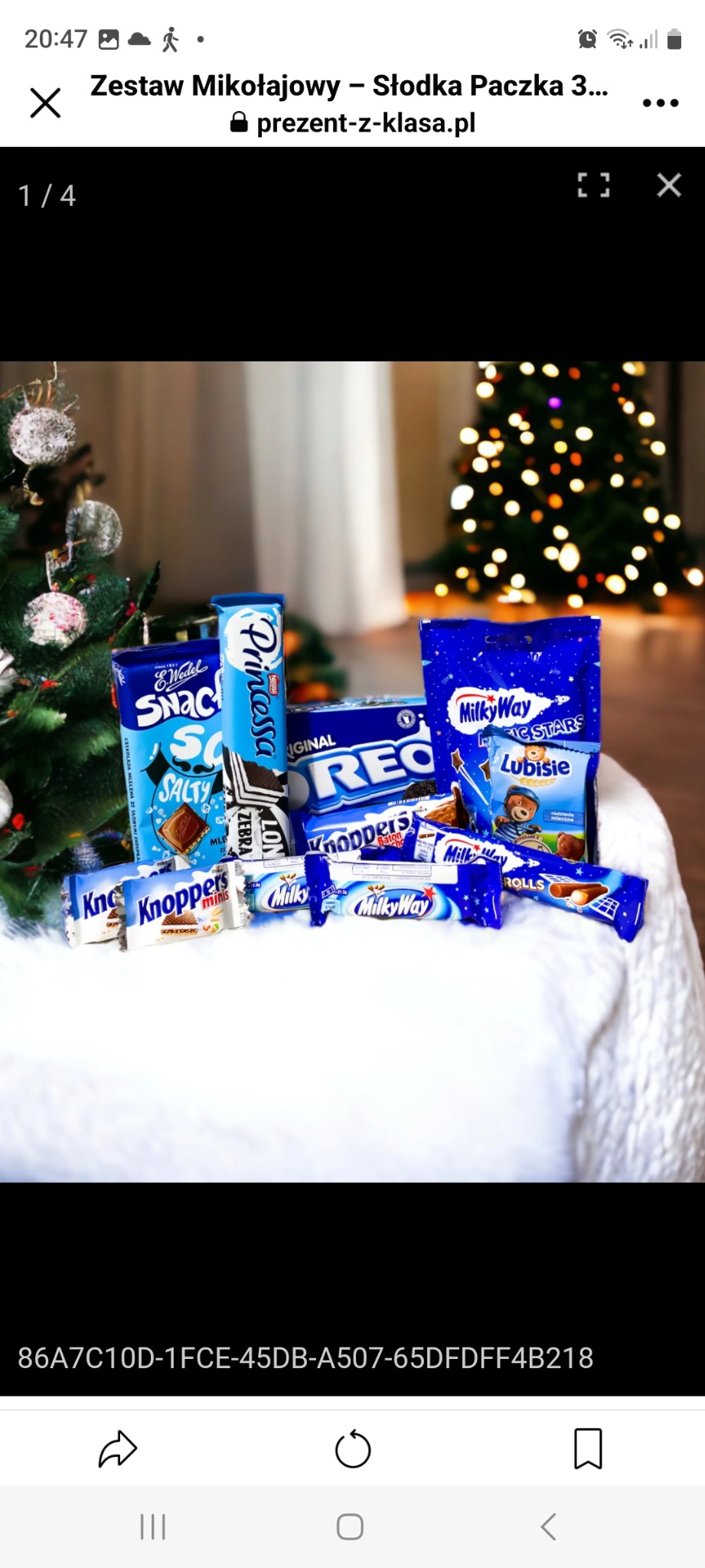 Słodki upominek z batonami i ciastkami Princessa, Oreo, Knoppers, Milky Way, Lubisie oraz Wedel Salty Snack, ułożony na białym puszystym materiale, z choinką w tle.